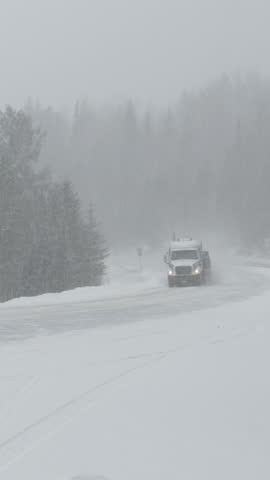 Cars and truck carefully move along a country road during a punishing snowstorm. Freight truck leads the way for other vehicles driving through a blizzard covering rural Canada with fresh snow.