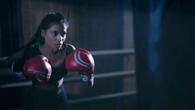 Indian young adult gen z woman in sportswear do sport training punching on black bag indoor place. Healthy athletic boxer female standing wear boxing gloves learn beat exercise workout at dark room - Powered by Shutterstock - Get 15% off with code: PIKWIZARD15