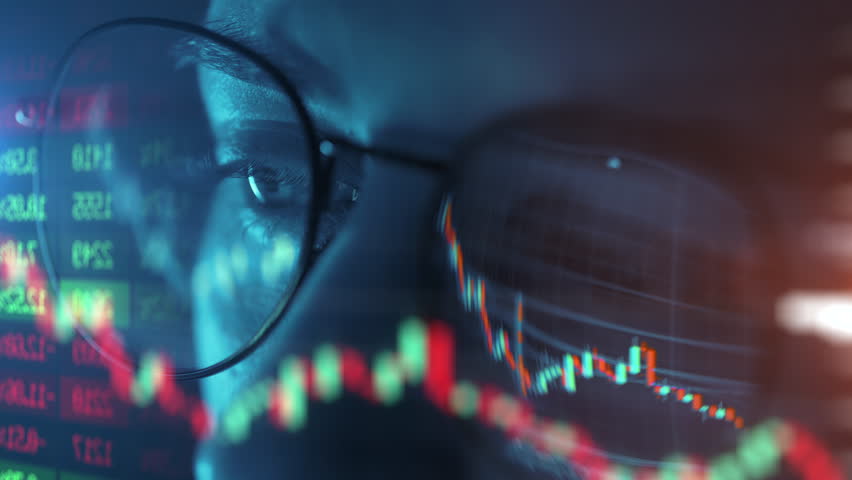 Trader wearing glasses is working on laptop computer. Screen with stock market charts and Bitcoin BTC or Ethereum ETH data analysis reflection. Broker trading online. Altcoins crypto currency trading