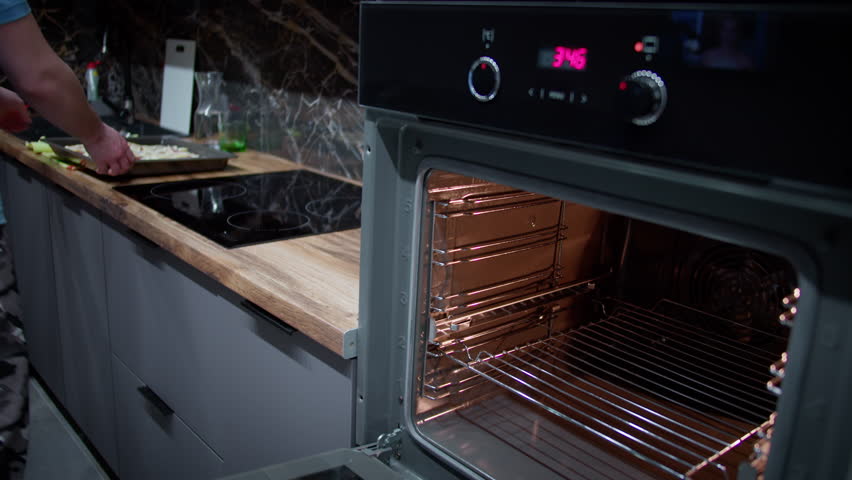 Man at home in kitchen making homemade pizza, putting baking tray in oven