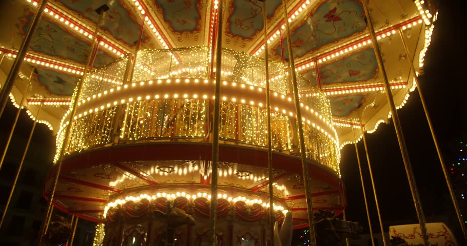 The illuminated carousel in the amusement park is spinning at night. The beautiful park is having fun