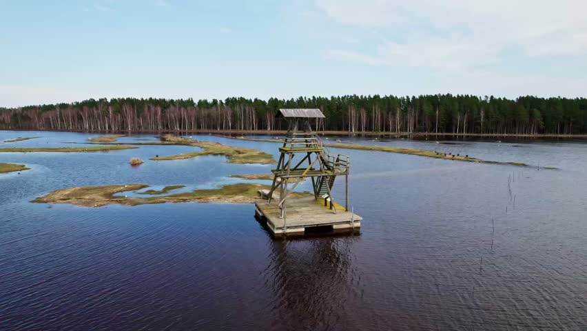Wooden observation tower in the middle of a lake with a forest in the background. Drone footage. Latvia