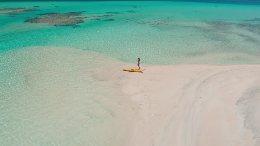 Woman enjoying a sunny day on a sandbank in a tropical paradise, surrounded by turquoise waters, clear skies, and fluffy clouds, evoking relaxation and freedom