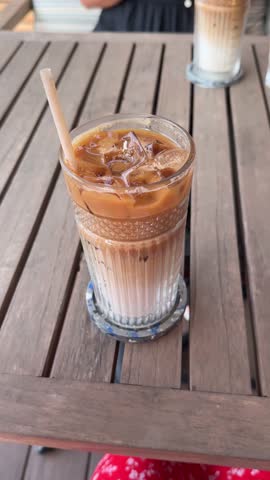Iced coffee stir in glass on table in cafe, closeup.girl hand wooden table ice latte cappuccino cold summer drink 