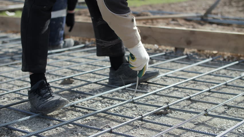 Worker fastening rebar grid for concrete foundation