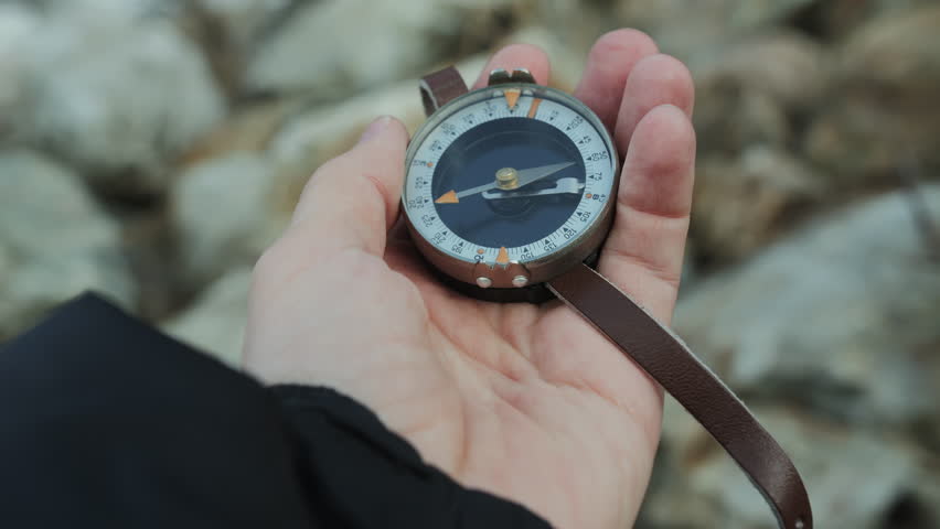 Hand holding a compass over rocky ground