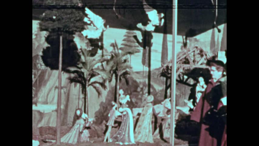 United States CIRCA United States 1950s: Group of children sit around Christmas tree and woman tells story. Wreath on wall. Lights on tree. Christmas lights on house. Reindeer decorations. 