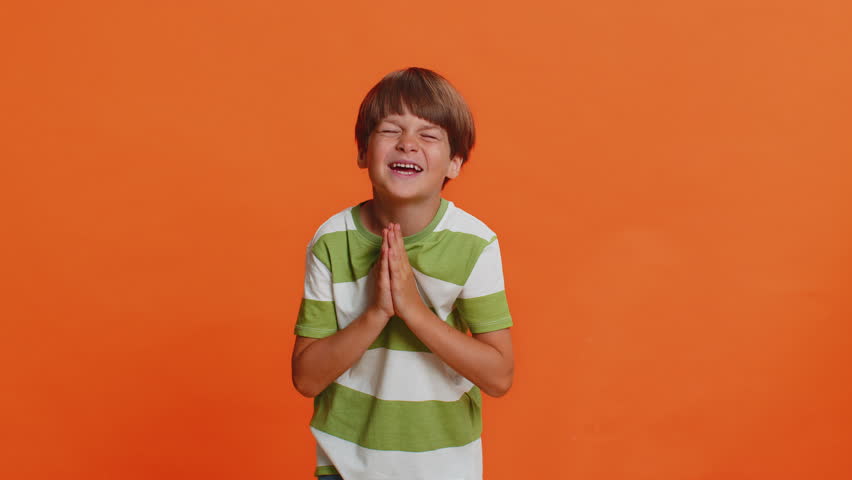 Please, God help. Preteen child boy kid praying making wish, asking with hopeful imploring expression, begging apology, asks not to punish him for bad behavior. Little children on orange background