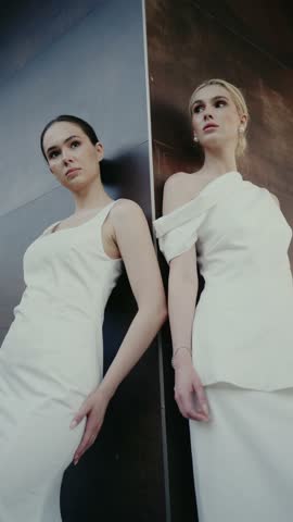 Two elegant women in stylish white dresses pose confidently against a modern background conveying sophistication and contemporary fashion. Elegant Women Posing in Stylish Dresses