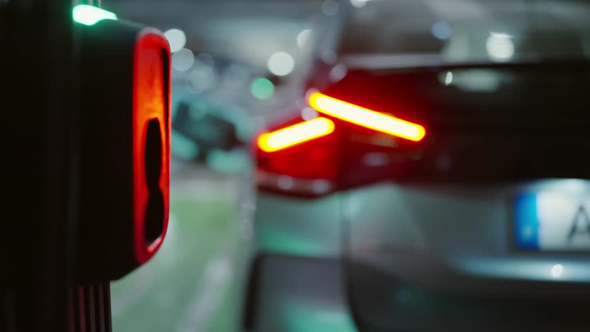 Close-up view of a hand plugging a charger into an electric vehicle in dimly lit conditions, emphasizing eco-friendly transportation and modern technology. Person Plugging in Electric Vehicle Charger