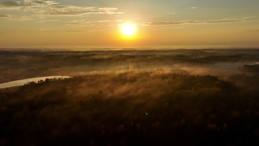 Beautiful dawn aerial shot of sunlight shining thought the trees and low fog in Minnesota in the autumn. Trees are turning their fall colors