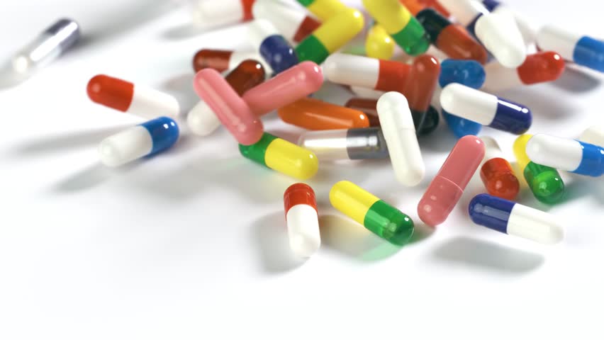 Colorful pills fall onto a white surface in slow motion.
