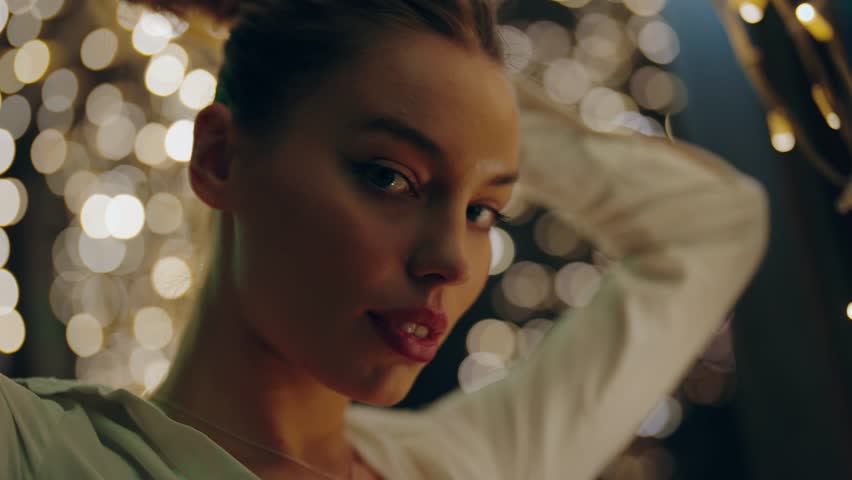 Woman posing gracefully in front of blurred festive lights, evoking a dreamy and contemplative mood during a nighttime celebration. The soft glow highlights her serene beauty and elegance.