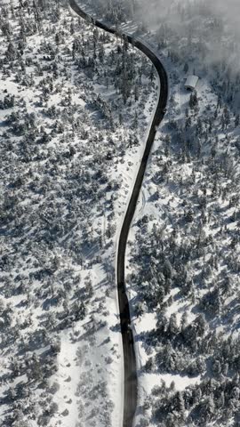Aerial of a road going through the snow covered San Bernardino Mountains near Los Angeles California. Vertical video.