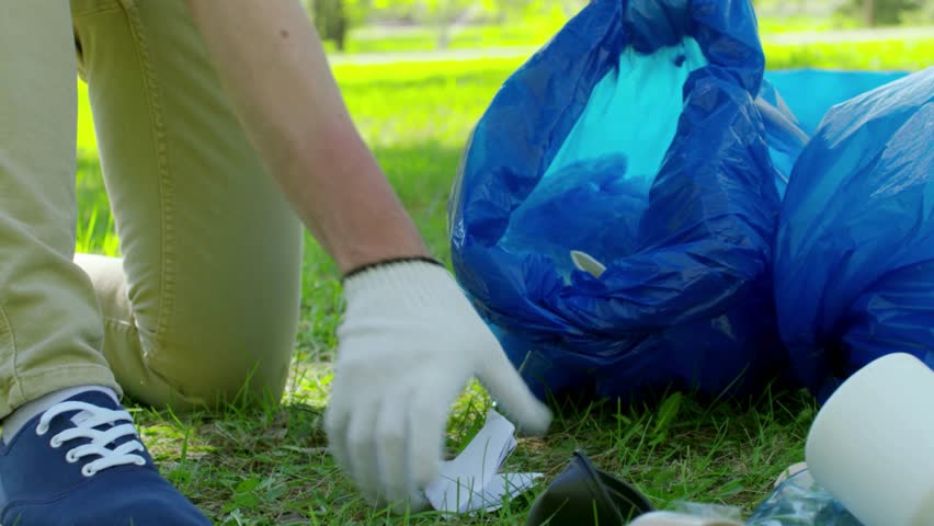 A person cleaning a garden by picking up garbage and removing litter from the grass and pathways. The video shows responsible environmental behavior and community involvement in maintaining a clean.