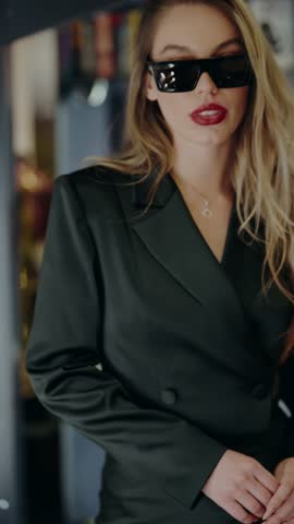 Elegant woman wearing a black suit and sunglasses, exuding confidence and style in an urban environment. Perfect for business, fashion, and lifestyle themes. Young Woman in Black Suit with Sunglasses