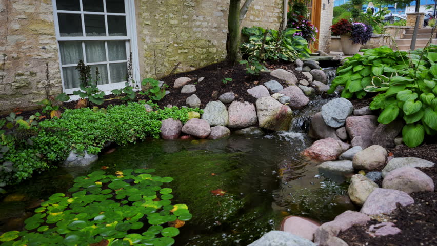 Cozy pond with lot of greenery and stones near the house.