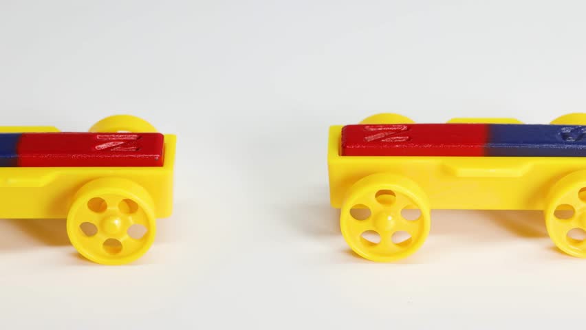 Hands manipulate yellow toy cars with red and blue magnets on a white surface.