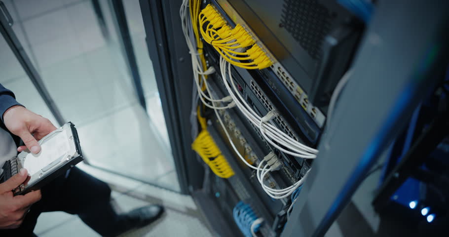 Server Technician Installing Additional Hardware into a Server Cabinet in a Data Center. Anonymous Specialist Inserting Hard Drives in Order to Increase Storage, Memory and Compute Power. High Angle