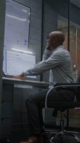 Happy Stock Trader Monitoring Real-Time Stocks on Computer, Having Phone Call, Celebrating Winning Trading Deal. Excited African American Investment Agent Making Profitable Investments. Vertical Shot.