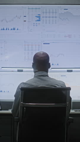 Stock Exchange Broker Monitoring Real-Time Stocks, Exchange Market Charts on Computer with Multi-Monitor Desktop Setup, Talking on Phone. African American Investment Agent in Office. Vertical Shot.