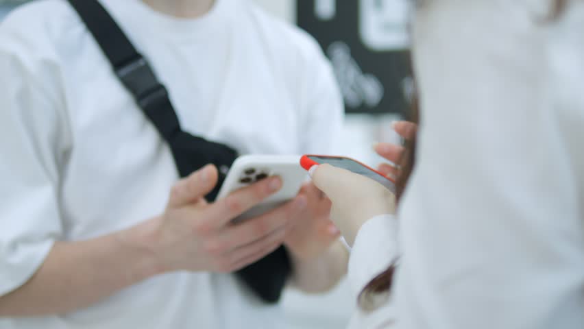 Man and a woman are standing next to each other, both holding cell phones. The man is wearing a white shirt and a black backpack. They are both looking at their phones