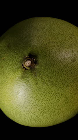 Two Hands Opening a Pomelo to Reveal Juicy Pale Segments Inside Thick Green Rind in Close-Up Against Black Background.
