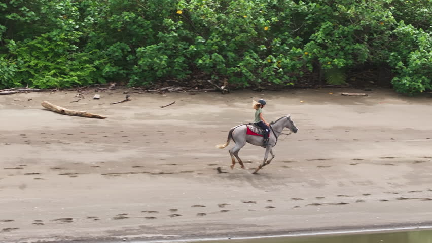 In Costa Ricas stunning landscape, a young girl rides her horse along the sandy shoreline in slow motion, showcasing their deep connection, joy, and freedom amidst the breathtaking coastal beauty