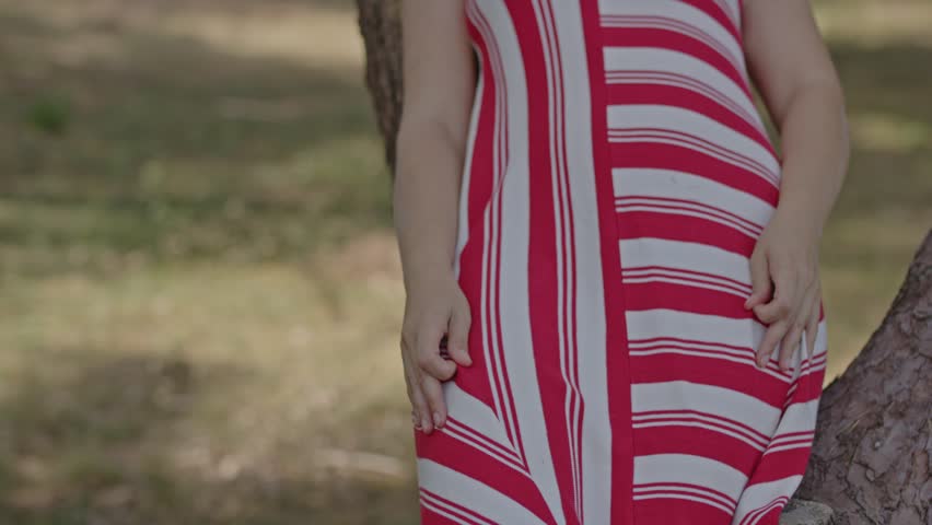 Close up of a beautiful summer dress being worn by a woman sitting on a tree in a sunny forest