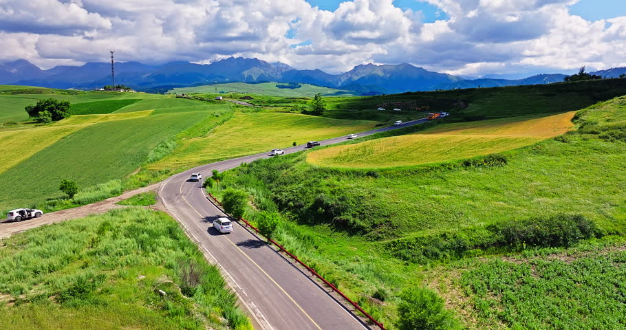 Country road and green wheat fields with mountain natural landscape in summer. Beautiful natural park scenery in Xinjiang, China.