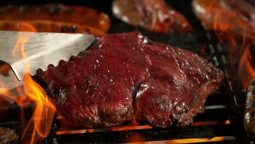 Super Slow Motion Shot of Flipping Beef Steak Meat on Hot Grill with Flames at 1000fps.