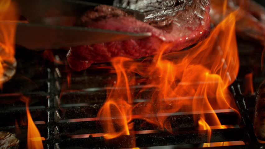 Super Slow Motion Shot of Flipping Beef Steak Meat on Hot Grill with Flames at 1000fps.