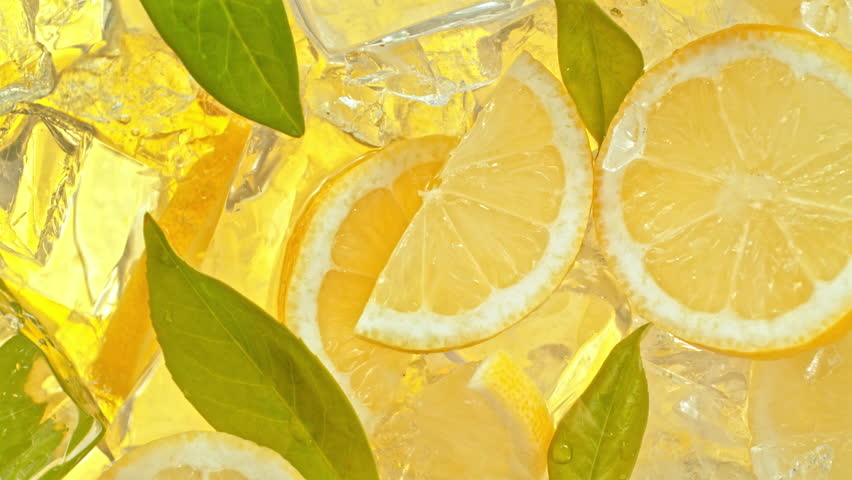 Super Slow Motion Shot of Pouring Lemonade on Fresh Lemon Slices, Ice and Green Leaves at 1000fps.