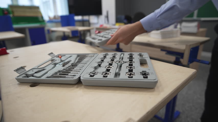 Teacher puts toolboxes on classroom desks preparing for practical lesson. Organized layout ensures each student has necessary equipment
