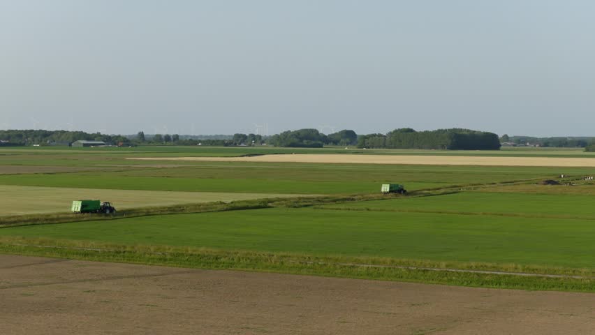 Tractors on green fields in flat Dutch nature reserve under calm, clear summer sky