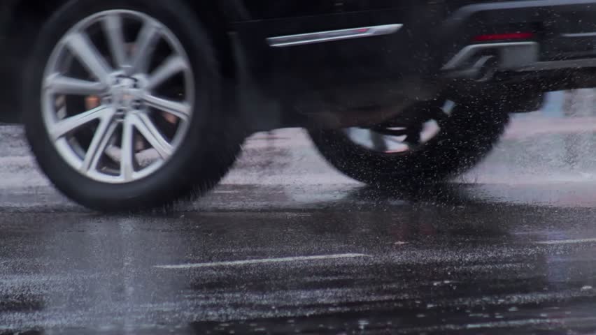 splashes from car wheels on the road while driving through puddles in the city after a hurricane in the fall. Cloudy weather, rainy season, flood on the road. Slow motion