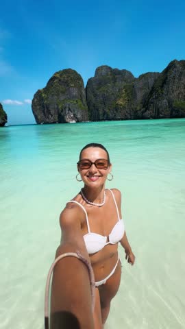 Joyful woman in white bikini captures selfies at the stunning turquoise waters of Maya Bay, Phi Phi Islands, Thailand. Perfect concept for influencer, travel, summer and lifestyle content.