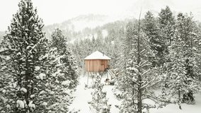 Drone flies through snowy trees toward stilted wooden cabin in Andorra, with snowfall and mountain backdrop. - Powered by Shutterstock - Get 15% off with code: PIKWIZARD15