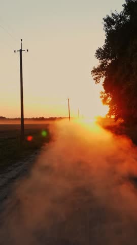 Dusty road. sunset over farm field. dusty, dirt road along an agricultural field and forest, at sunset. dust rises in the air. dust clouds rise