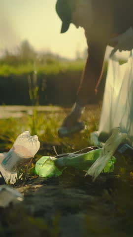 A young man is actively collecting and sorting plastic waste along the shore of a pond. This cleanup effort takes place during the daytime, highlighting the urgency of environmental protection