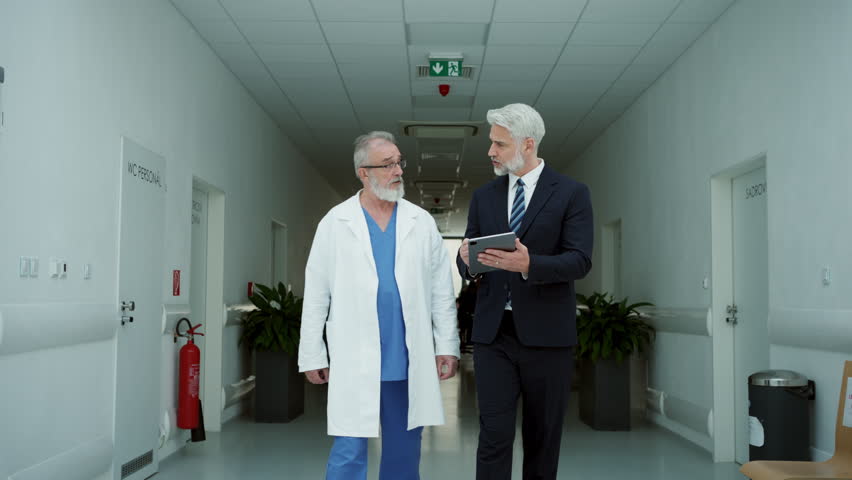 Medical sales representative presenting new medication to doctor, walking through corridor in hospital.