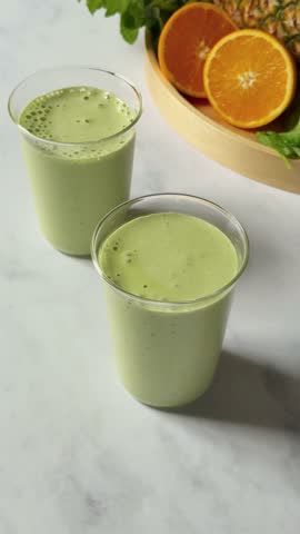 Vertical video of a green smoothie with fruit and gold straw on marble table, health wellness foodie shoot