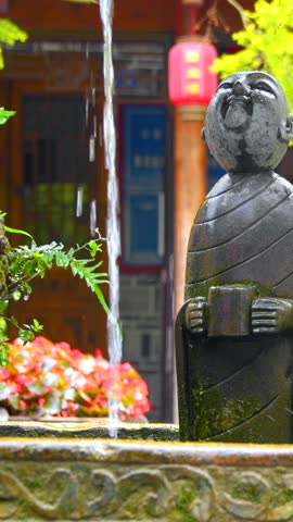 An ancient stone figure facing an artificial waterfall, Huanglongxi Ancient Town, Chengdu, Sichuan, China