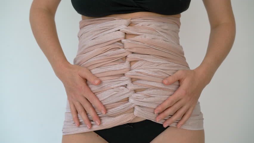 Close-up of postpartum woman's belly wrapped in traditional bengkung belly binding cloth, symbolizing healing and support after childbirth in natural way.