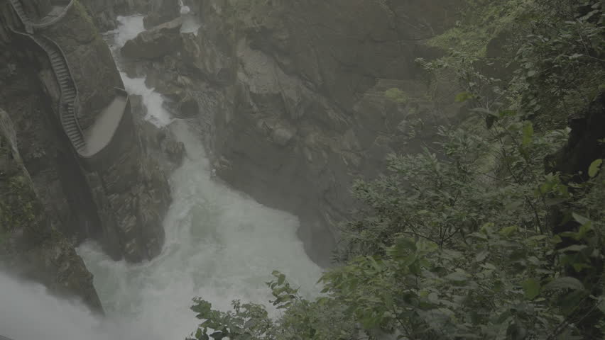 A top view of Pailon del Diablo Waterfall in Banos, Ecuador, powerful waters plunging through lush green cliffs and rocky terrain