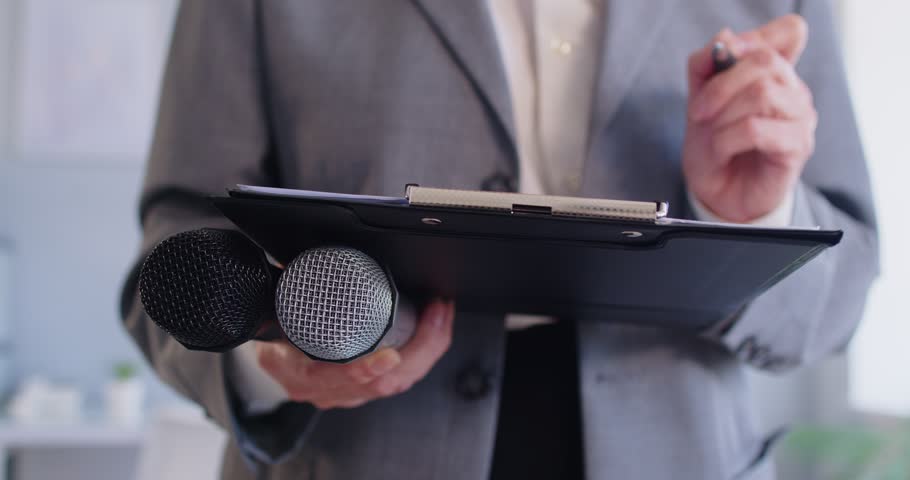 Female journalist writing on notepad. Cropped closeup woman reporter holding clipboard and microphones taking article notes or preparing questions for interview. Media, journalism, press, news concept