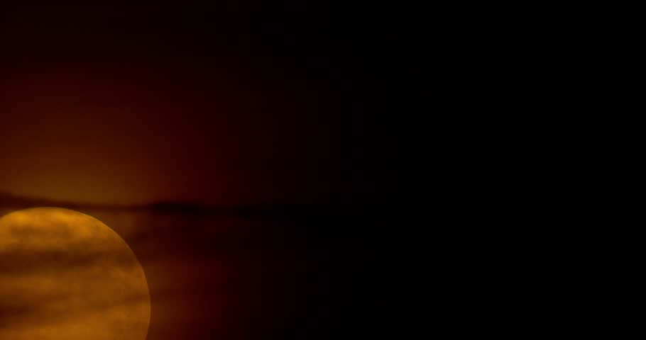 A telescopic timelapse of a full moon rising and glowing through a dark sky until it fades out