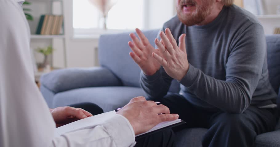 Professional psychologist doctor making notes consulting senior elderly man patient sitting on sofa during therapy session in office. Psychotherapy, psychology and mental health concept. 4k video.