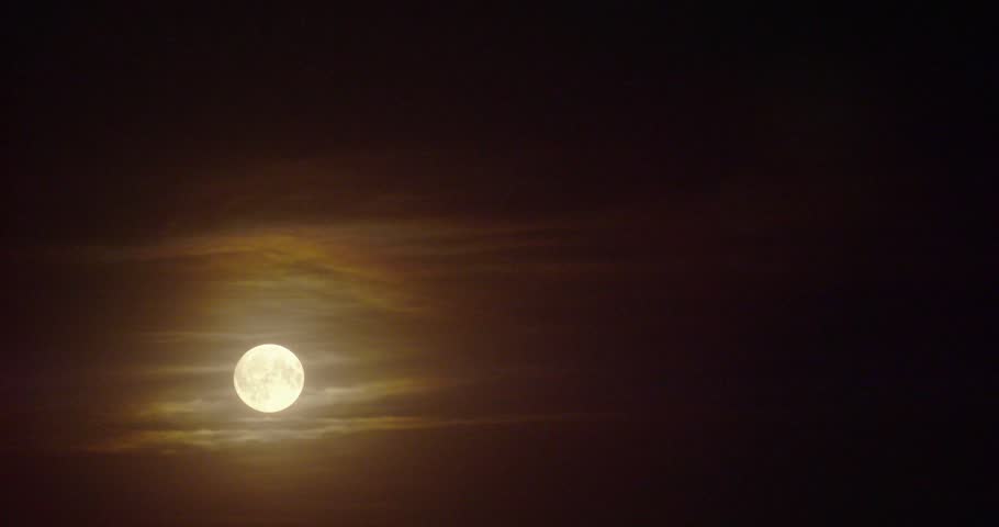 A mesmerizing timelapse of a glowing moon moving in dark sky with smooth clouds