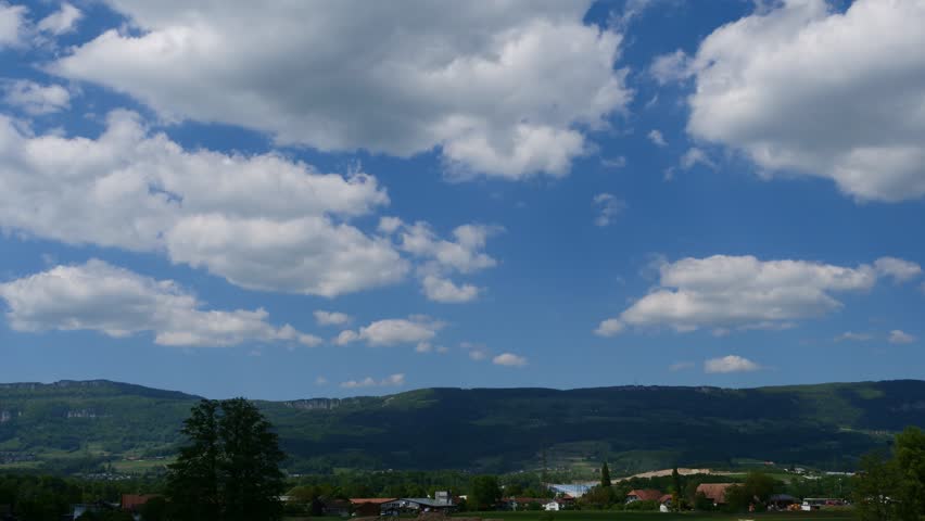 A time-lapse footage of the white puffy clouds rolling in the blue sky over a rural village on a sunny day, in Deitingen, Solothurn in Switzerland